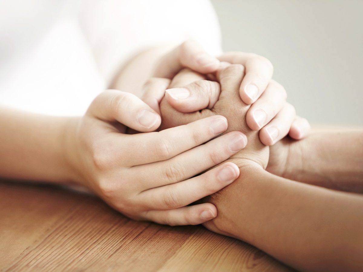 Two people holding hands in a supportive counselling setting
